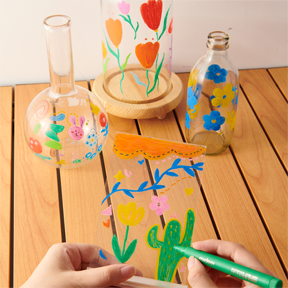 Hands using Acrylic Markers with Ultra Soft Nib to create vibrant illustrations on varied glass surfaces, demonstrating versatility and color quality