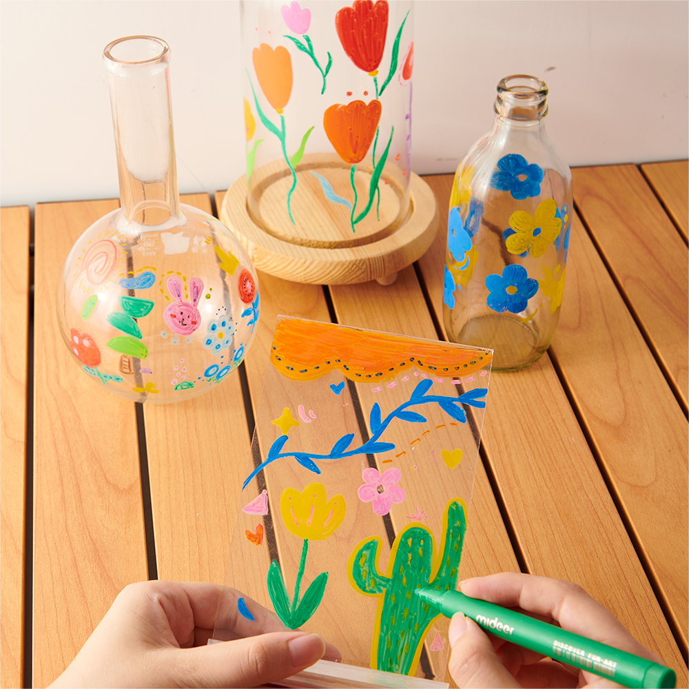 Hands using acrylic markers with ultra soft nib to create vibrant designs on glass surfaces, showcasing versatility on different materials