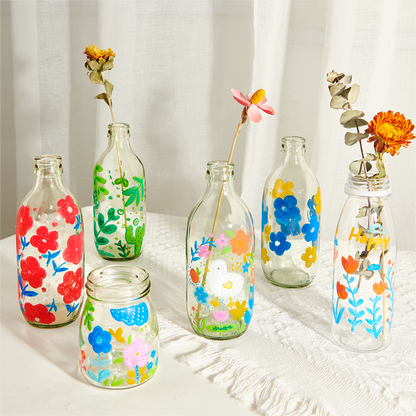Assorted glass bottles artistically decorated with vibrant flowers and patterns using ultra-soft nib acrylic markers, showcasing versatile application on smooth surfaces