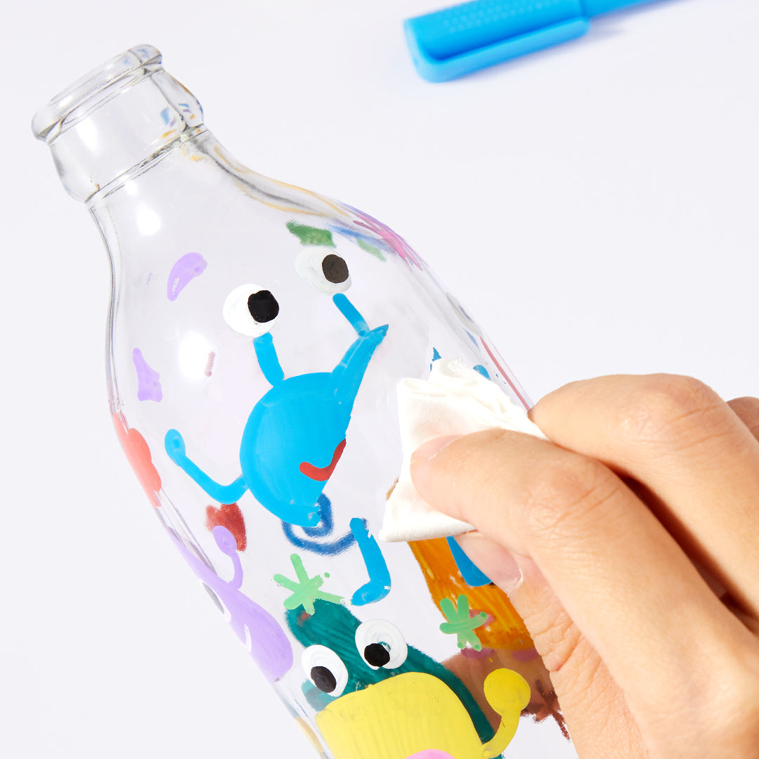 Hand using round nib acrylic marker for crafting on a clear glass bottle, demonstrating versatility on various surfaces